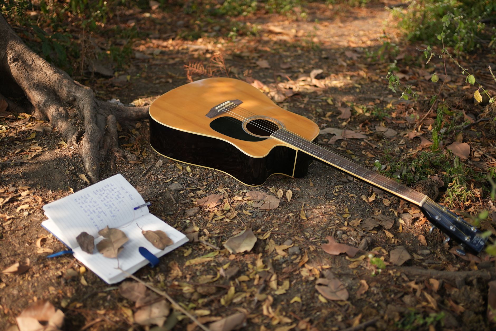 An acoustic guitar beside an open notebook of handwritten lyrics